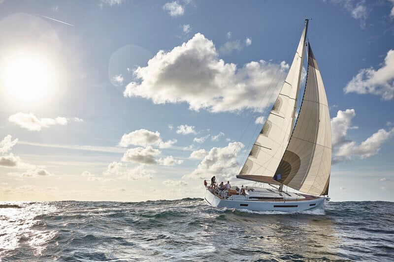 Sun Odyssey 490 - purjevene seilaa auringonpaisteessa, miehistö ohjaa venettä vakaasti merenkäynnissä.