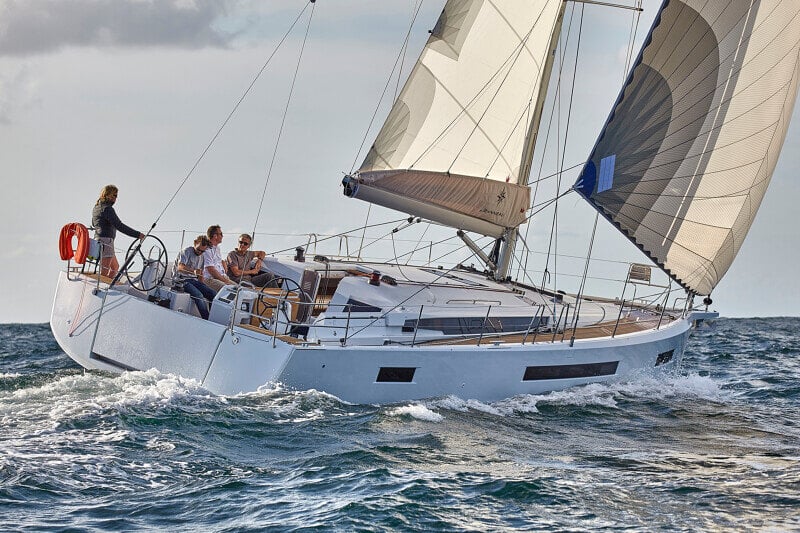 Sun Odyssey 490 - rentoutumista kannella, jossa seurue nauttii auringosta ja merinäköalasta kaupunkisiluettia vasten.