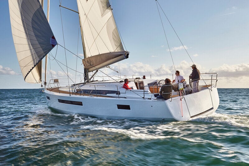 Sun Odyssey 490 - merellä purjehtiva luksusvene, jossa matkustajat rentoutuvat ja ohjaaja hallitsee venettä.