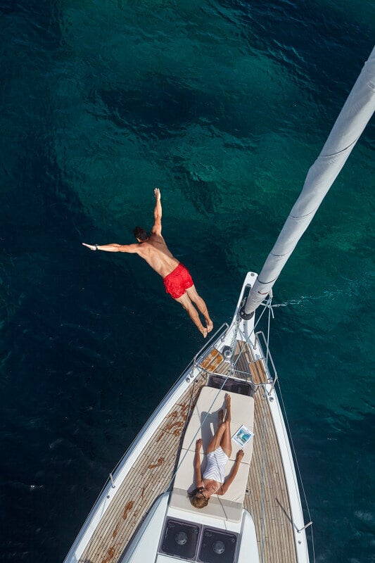 Sun Odyssey 490 - mies hyppää veteen veneen keulasta, kun nainen nauttii auringosta kannella.