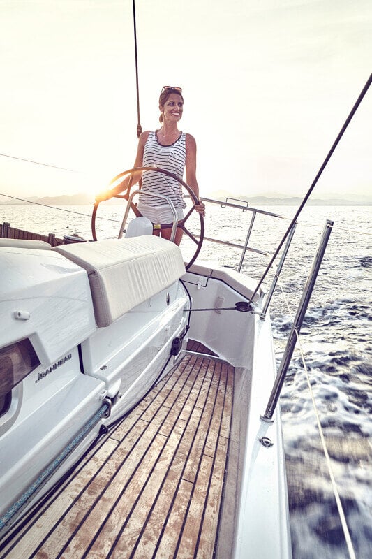 Sun Odyssey 490 - nainen ohjaamassa purjevenettä tyylikkäästi suunnitellulla avotilalla auringonlaskun aikaan.