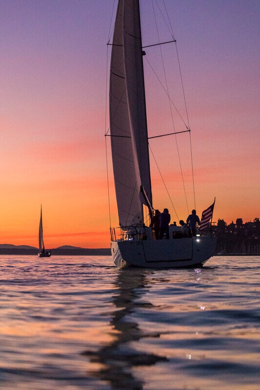 Sun Odyssey 490 - purjevene purjehtii auringonlaskun aikaan, taivaan värit heijastuvat veden pinnalle.