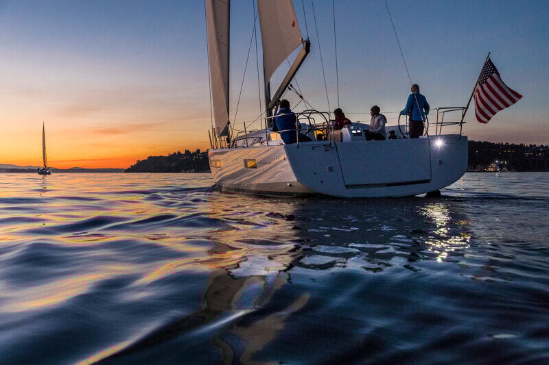 Sun Odyssey 490 - purjevene iltahämärässä kaupungin siluetin edessä, täysikuu valaisee tyynen veden.