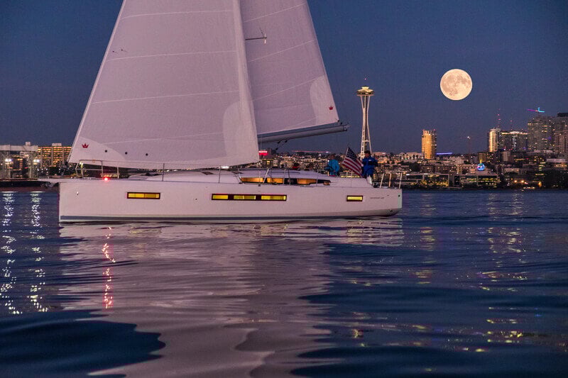 Sun Odyssey 490 - purjevene auringonlaskussa, pehmeät värit heijastuvat veden pintaan.