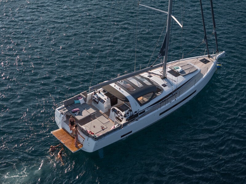 Ylhäältä kuvattu Jeanneau Yachts 55, jossa miehistö ja matkustajat nauttivat peräkannen mukavuuksista ja uimatasosta.