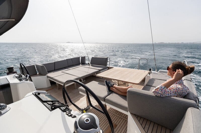 Nainen seisoo Jeanneau Yachts 55:n kannella katsellen horisonttia, nauttien purjehduksen vapaudesta ja merituulesta.