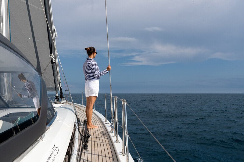Nainen seisoo Jeanneau Yachts 55:n kannella katsellen horisonttia, nauttien purjehduksen vapaudesta ja merituulesta.