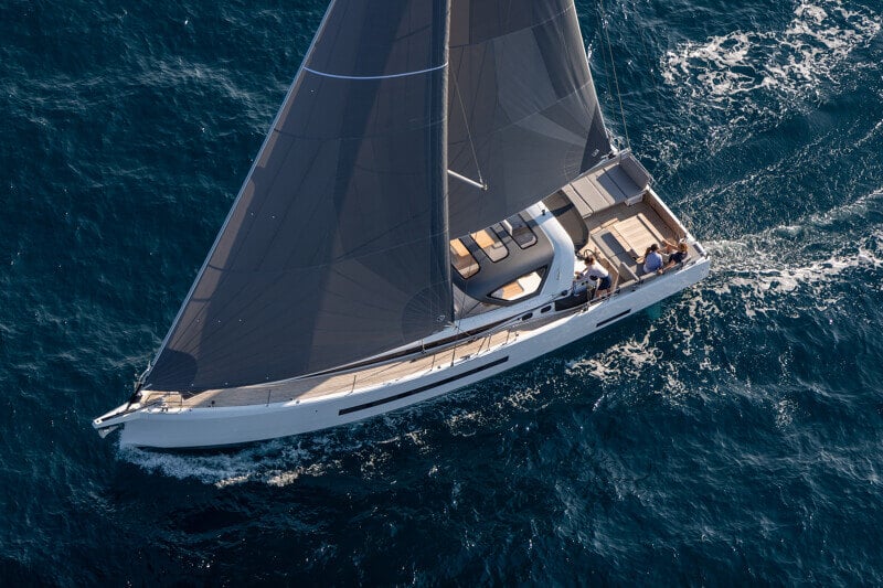 Ilmakuva Jeanneau Yachts 55:stä ankkurissa, jossa matkustajat rentoutuvat tilavalla kannella nauttien auringosta.