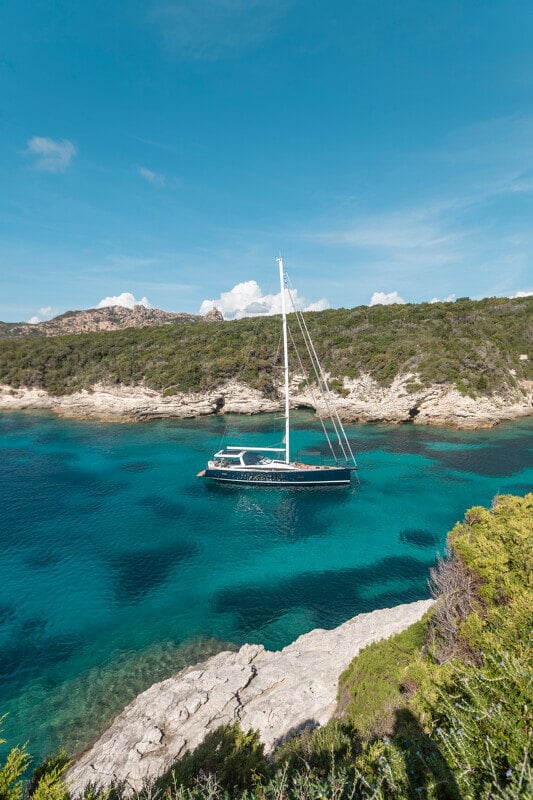Jeanneau Yachts 65 ankkuroituna kallioisen saaren edustalla, kirkasta vettä ympärillä.
